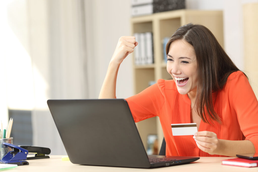 Comprador eufórico comprando online com um laptop e um cartão de crédito em casa.