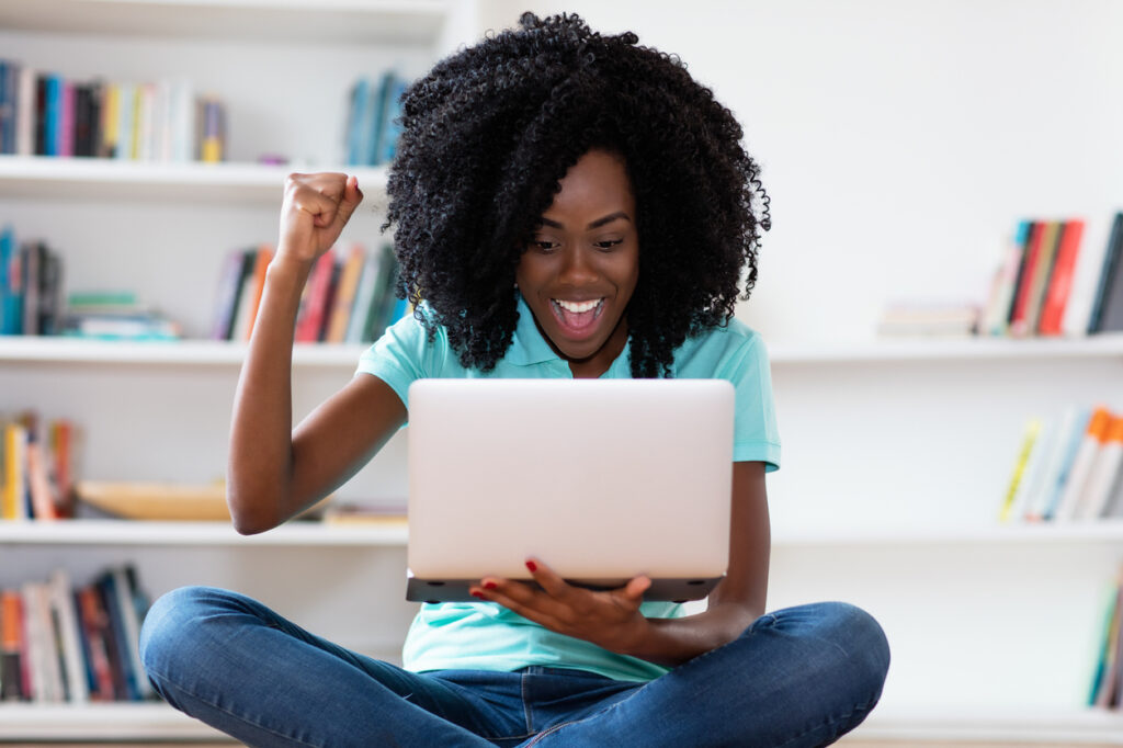 Mulher afro-americana fazendo compras online com o computador em casa, umas das maneiras de ganhar milhas aéreas.