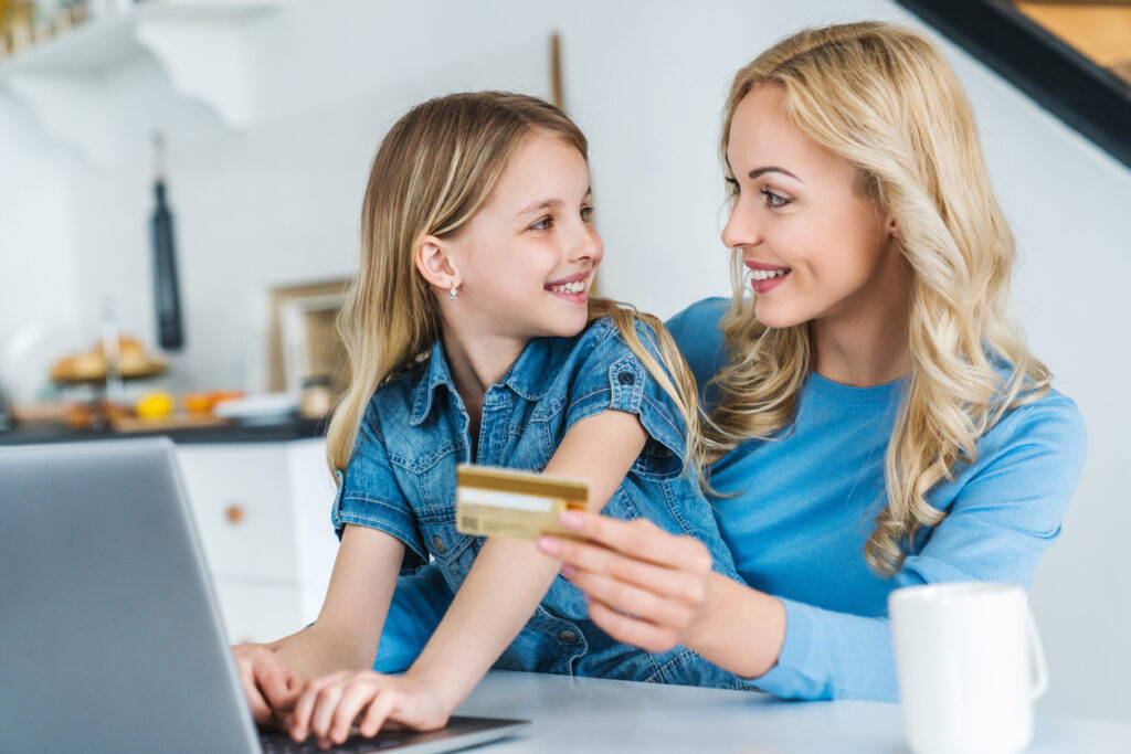 Jovem mulher caucasiana fazendo compras online usando cartão de crédito com a filha em casa.