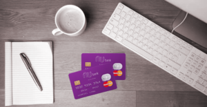 Imagem de cartão de crédito Nubank junto ao notebook, xícara e bloco de notas e caneta. Conheça como funciona o NuBank Rewards.