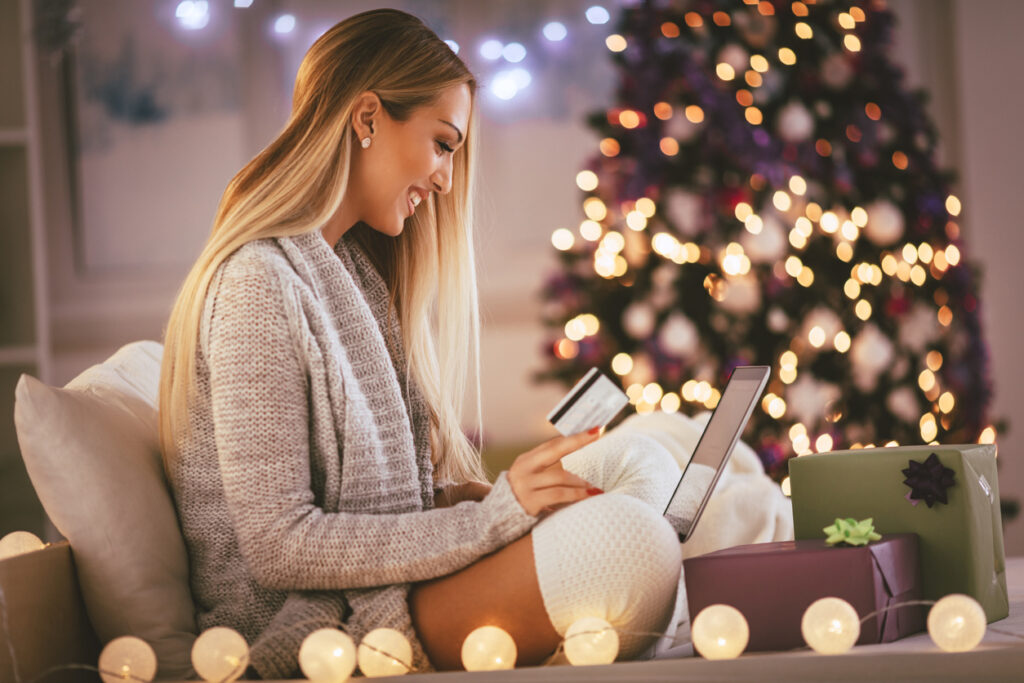Mulher jovem feliz relaxando em casa e comprando online presentes de Natal no laptop depois de vender milhas e ter um bom lucro..