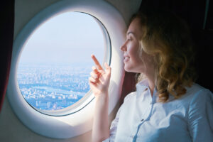 Mulher passageira de avião com interesse olha para a cidade abaixo. Mulher escolhe melhor companhia aérea para viajar e acumular mais milhas para vender.